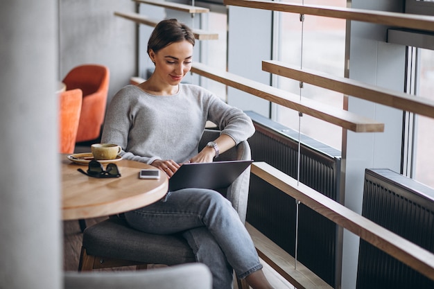 Femme assise dans un café, buvant du café et travaillant sur un ordinateur