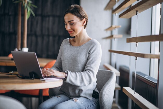 Femme assise dans un café, buvant du café et travaillant sur un ordinateur