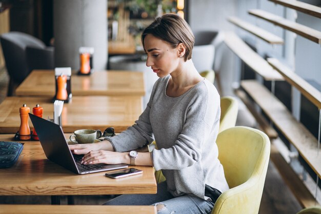 Femme assise dans un café, buvant du café et travaillant sur un ordinateur