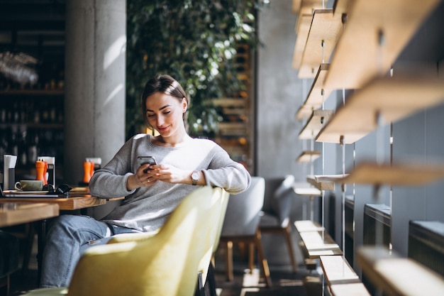 Femme assise dans un café, buvant du café et travaillant sur un ordinateur