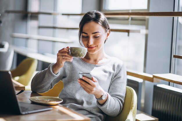 Femme assise dans un café, buvant du café et travaillant sur un ordinateur