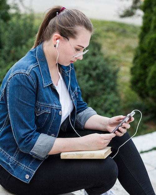 Femme assise dans le parc en utilisant un smartphone