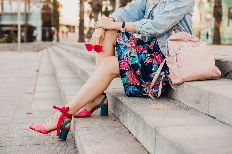 Photo gratuit femme assise sur les escaliers dans la rue de la ville en jupe imprimée avec sac à dos en cuir tenant des lunettes de soleil