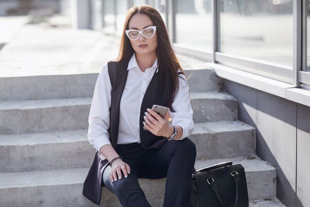 Femme assise sur les escaliers en regardant son téléphone