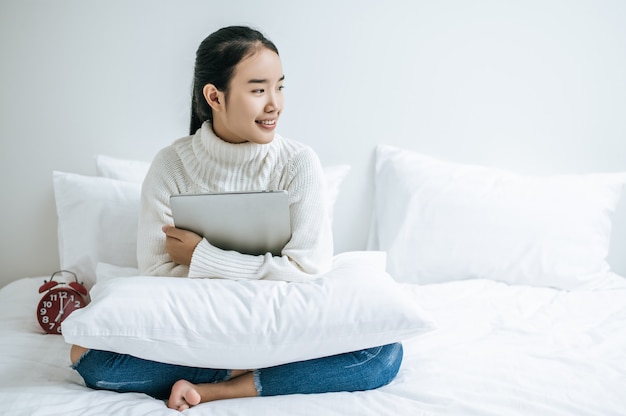 Une femme assise sur le lit, étreignant l'ordinateur portable et souriant.