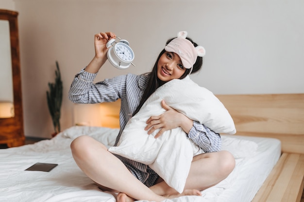 Photo gratuite femme assise sur le lit et étreint un oreiller