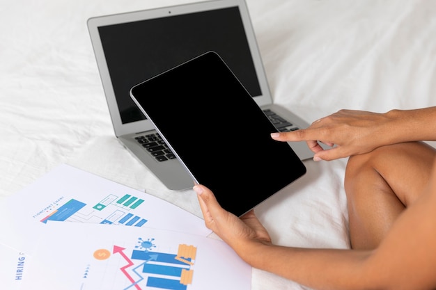 Femme assise sur le lit avec ordinateur portable et tablette