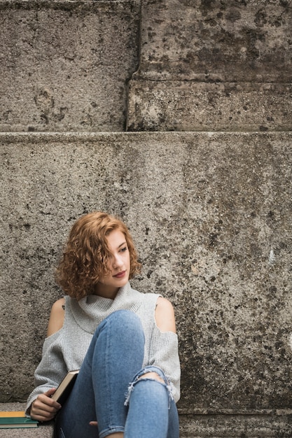 Femme assise près de mur de pierre