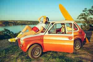 Photo gratuite femme assise et reposant sur la voiture sur la plage un jour d'été près de la rivière.