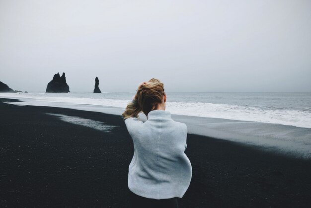 Femme assise sur le rivage près de l'eau avec un ciel nuageux en arrière-plan tourné par derrière