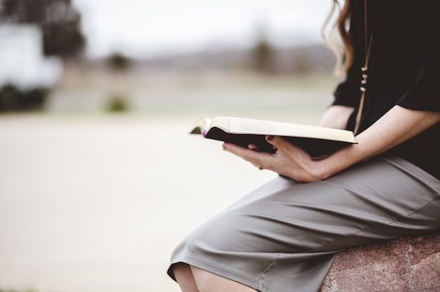 Femme assise sur un rocher à l'extérieur en lisant un livre