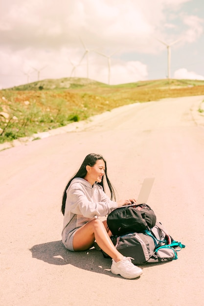 Femme assise sur la route et travaillant sur un ordinateur portable placé sur des sacs à dos