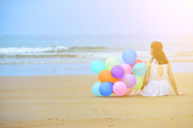 Femme assise sur le sable à côté d&#39;un bouquet de ballons