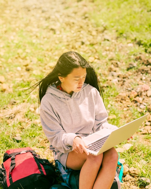 Femme assise sur un sac à dos et travaillant dans un ordinateur portable