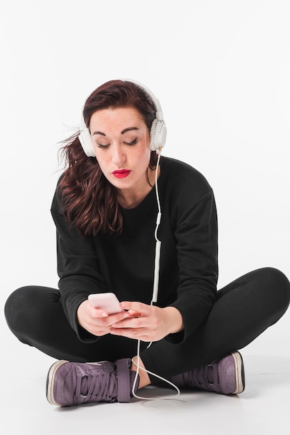 Photo gratuite femme assise sur le sol, écoute de la musique à travers un casque blanc