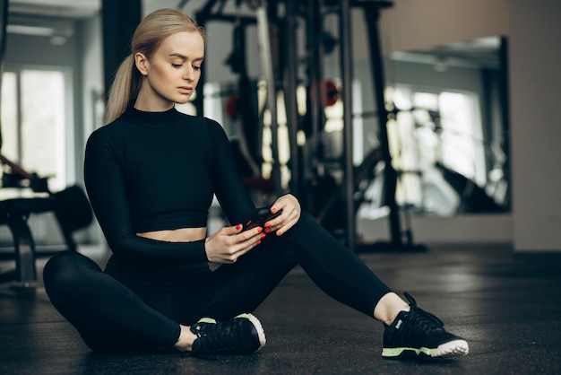 Femme assise sur le sol à la salle de sport et utilisant un téléphone portable