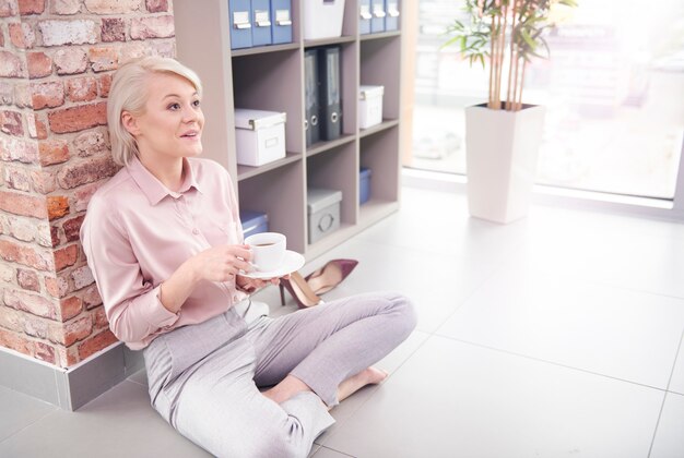 Femme assise sur le sol avec une tasse de café au bureau