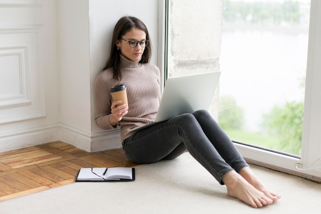 Femme assise sur le sol travaillant sur son ordinateur portable