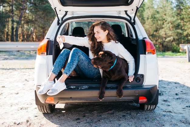 Femme assise avec son chien dans le coffre ouvert