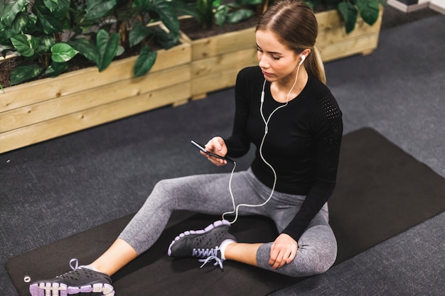 Femme assise sur un tapis d&#39;exercice en écoutant de la musique