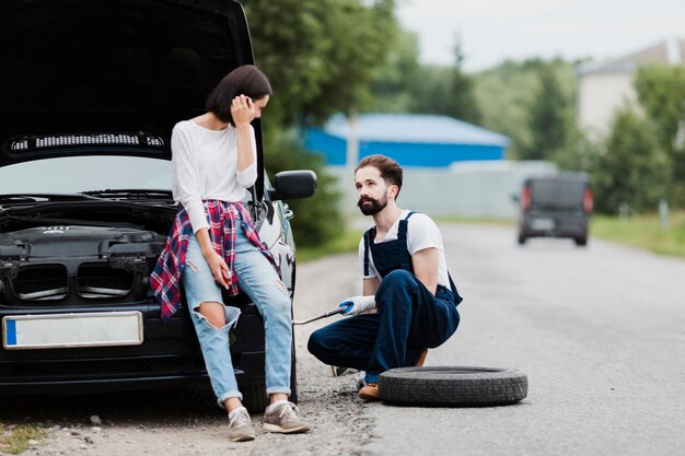 Femme assise sur la voiture et l'homme change de pneu