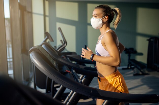 Femme athlétique avec masque facial courant sur tapis roulant dans un club de santé