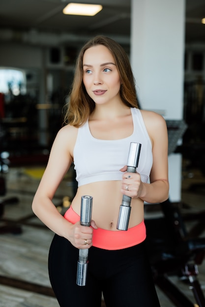 Femme athlétique pompage des muscles avec des haltères dans le club de gym