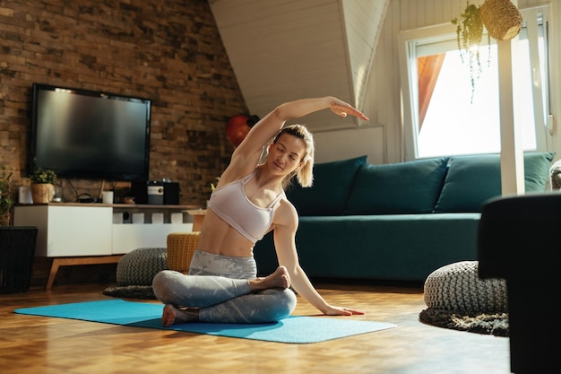 Femme athlétique s'échauffant tout en faisant des exercices d'étirement sur le sol à la maison