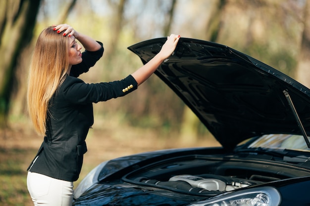 Une femme attend de l'aide près de sa voiture en panne sur le bord de la route.