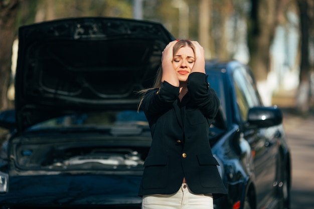 Une femme attend de l'aide près de sa voiture en panne sur le bord de la route.