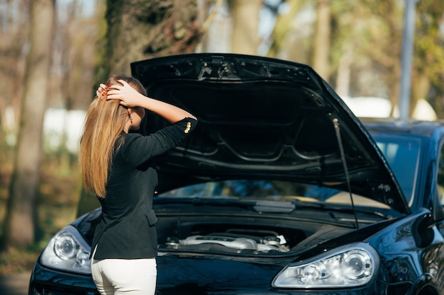 Une femme attend de l'aide près de sa voiture en panne sur le bord de la route.