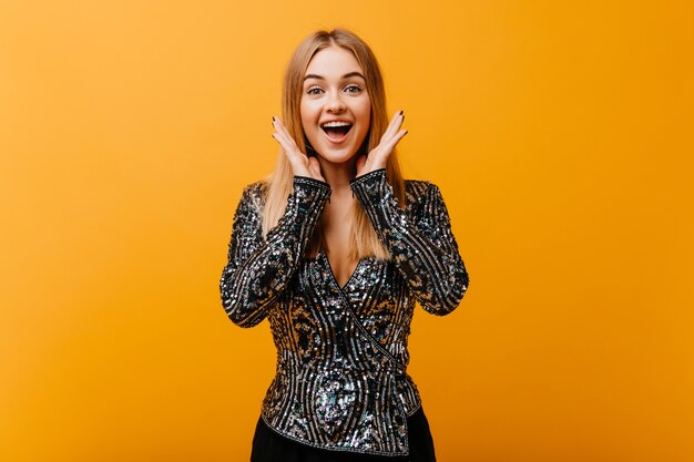 Femme attrayante en veste de soirée souriant sur orange. Modèle féminin Debinair exprimant le bonheur.