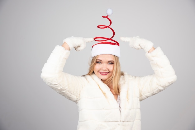 Femme au bonnet de Noel à la recherche d'heureux sur le mur gris.