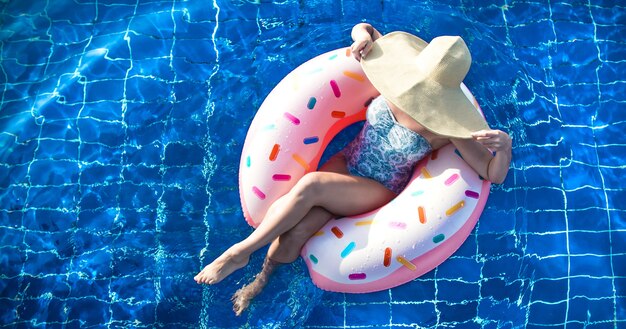 Une femme au chapeau se détend sur un cercle gonflable dans la piscine.