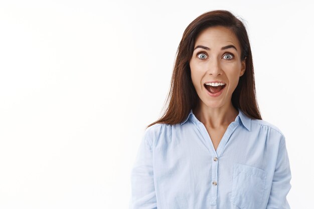 Une femme au foyer adulte joyeuse et amusée a l'air impressionnée, la bouche ouverte est fascinée, surprise, souriante excitée, participe à un événement intéressant, regarde devant elle, se demande un mur blanc enthousiaste