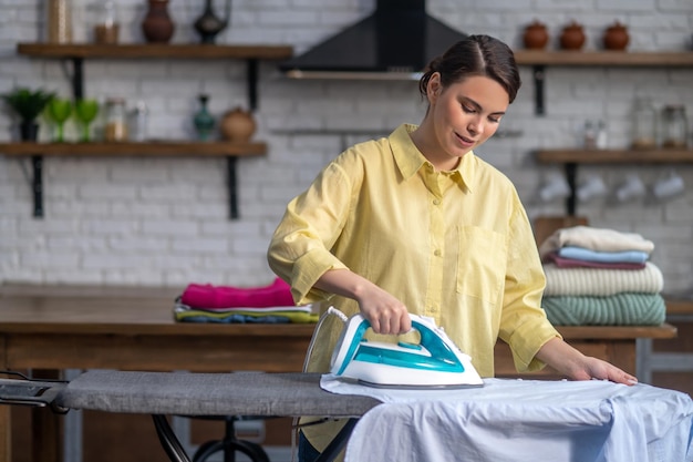 Femme au foyer concentrée repassant des vêtements froissés sur la planche à repasser