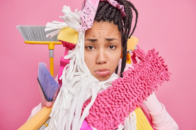femme au foyer entourée de matériel de nettoyage a l'air fatiguée et mécontente ne veut pas nettoyer la pièce marre du travail domestique isolé sur rose
