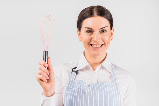 Femme au foyer souriante et tenant un fouet