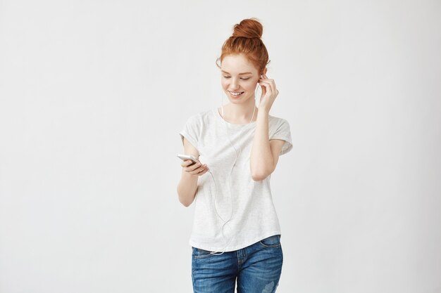 Femme au gingembre avec des taches de rousseur dans les écouteurs souriant regardant le téléphone.