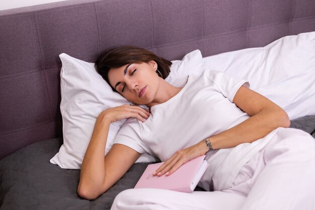 Femme au lit est tombé endormi tenant un bloc-notes pour ordinateur portable en papier 2021
