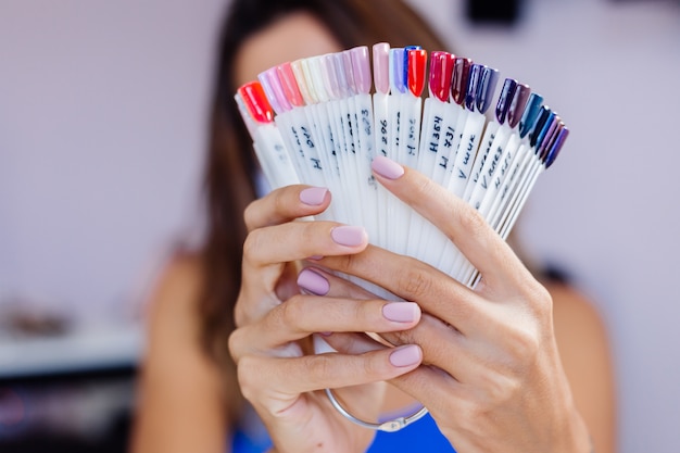 Femme au masque médical de protection dans un salon de beauté, maintenez la palette et sélectionnez une couleur Procédure de manucure Soins des ongles Ouverture officielle La quarantaine est terminée Les petites entreprises sont à nouveau ouvertes