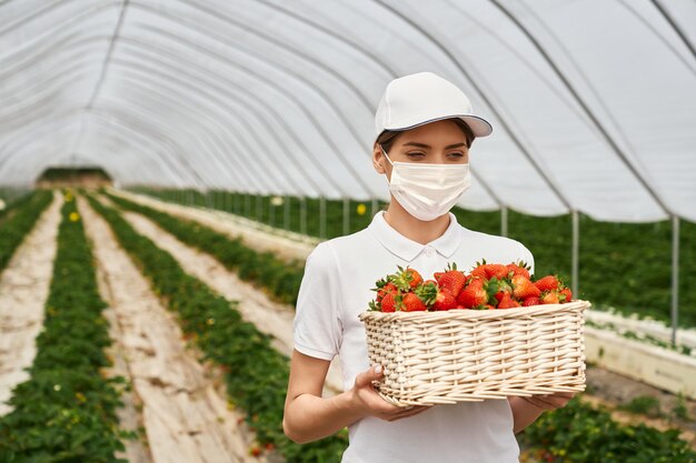 Femme au masque portant un panier avec des fraises