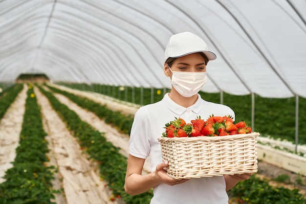 Femme au masque portant un panier avec des fraises