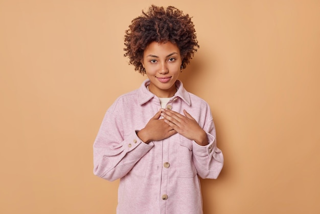 une femme aux cheveux bouclés apprécie un beau geste exprime sa gratitude pour quelque chose qui porte une veste décontractée touchée isolée sur beige. Je te suis vraiment reconnaissant