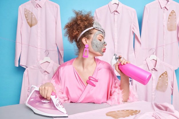 Femme aux cheveux bouclés détient un spray détergent occupé avec un masque d'argile.