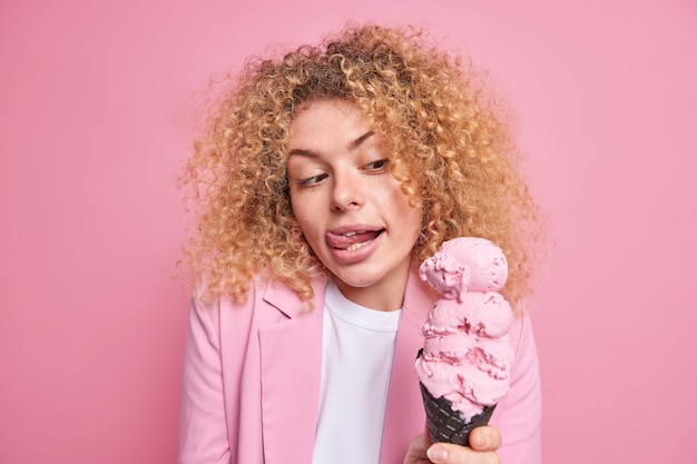 une femme aux cheveux bouclés lèche les lèvres avec la langue regarde une glace appétissante au cône ressent la tentation de manger un délicieux dessert d'été glacé après le travail vêtu de vêtements formels.