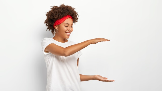 Photo gratuite femme aux cheveux bouclés montre la hauteur de quelque chose, fait des gestes avec les deux mains, montre la taille du paquet