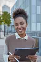 Photo gratuite une femme aux cheveux bouclés tient un stylo électronique et une tablette crée du contenu web via une application multimédia sur un pavé tactile recherche le site web pour discuter en ligne