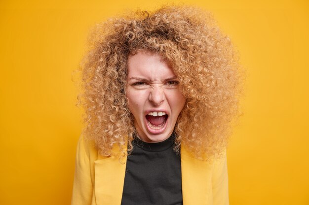 une femme aux cheveux bouclés et touffus crie avec colère a une querelle exprime des émotions négatives porte des vêtements formels