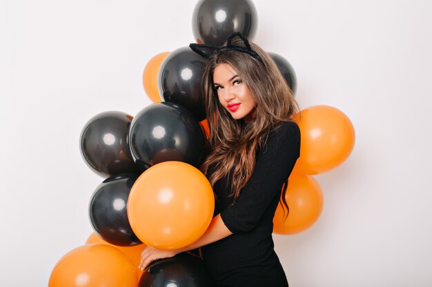 Femme aux cheveux bruns en robe élégante posant avec des ballons d'halloween